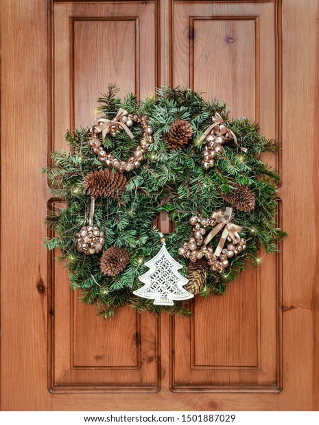 New Year and Christmas decor. Ornament a wreath from branches ate with cones, lights of a garland and gold spheres. Traditional Christmas decoration for interior and exterior.